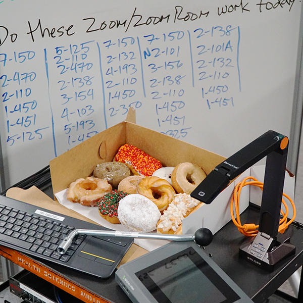 Box of donuts surrounded by AV equipment and a whiteboard of classroom names