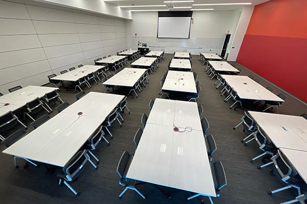 large classroom with projection screen, 16 tables of 8 with mics, and a closed folding wall